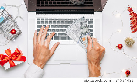 Online christmas shopping. Gift box red ribbon, trolley and laptop, dollar in flat lay internet online shopping composition. Winter Xmas holidays sales. 84554485