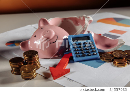 A broken piggy with stuck of coins, calculator and arrow down on business diagram. Business concept A broken piggy with stuck of coins, calculator and arrow down on business diagram. Business concept 84557983