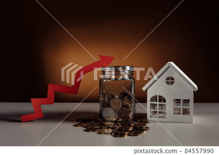 Glass jar filled coins, a red up arrow and house. The concept of the rising price of real estate Glass jar filled coins, a red up arrow and house. The concept of the rising price of real estate 84557990