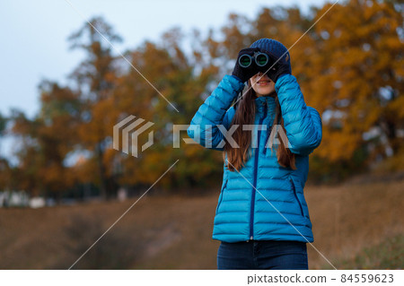 Young woman with binoculars watching birds in autumn park 84559623