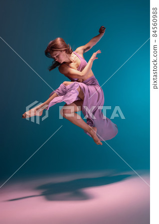 One young flexible contemp dancer in lilac dress dancing isolated on gradient blue white background in neon. 84560988