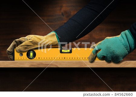 Manual Worker Holding an Orange Spirit Level on a Wooden Plank Manual Worker Holding an Orange Spirit Level on a Wooden Plank 84562660