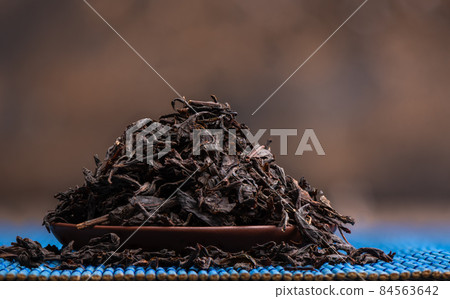 Close-up of dried tea leaves on a clay saucer over a blue mat. 84563642