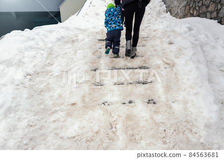 People walk by concrete stone staircase covered dirty deep slippery snow after blizzard snowstorm snowfall at city pedestrian walkway. Slide fall injury danger slip steps. Winter cold season weather People walk by concrete stone staircase covered dirty deep slippery snow after blizzard snowstorm snowfall at city pedestrian walkway. Slide fall injury danger slip steps. Winter cold season weather 84563681