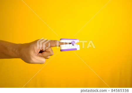 close up of man hand using pulse oximeter against yellow background close up of man hand using pulse oximeter against yellow background 84565336