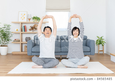 Middle-aged couple doing gymnastics in the living room at home Middle-aged couple doing gymnastics in the living room at home 84565485