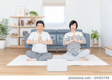 Middle-aged couple doing online yoga in their living room Middle-aged couple doing online yoga in their living room 84565748