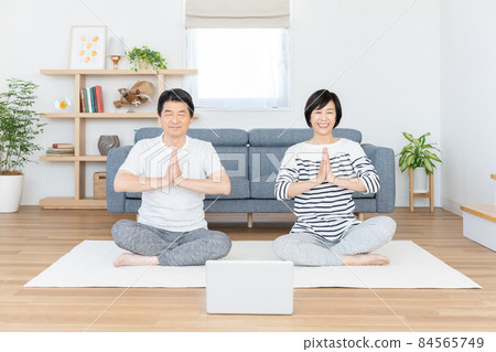 Middle-aged couple doing online yoga in their living room Middle-aged couple doing online yoga in their living room 84565749