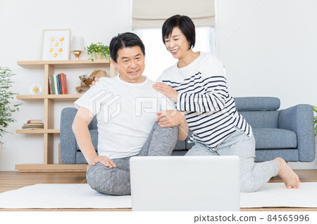 Middle-aged couple doing gymnastics online in their living room Middle-aged couple doing gymnastics online in their living room 84565996