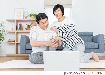 Middle-aged couple doing gymnastics online in their living room 84565997