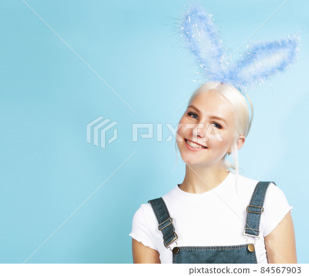 young pretty blond girl with rabbit ears posing cheerful on blue background, lifestyle people concept 84567903