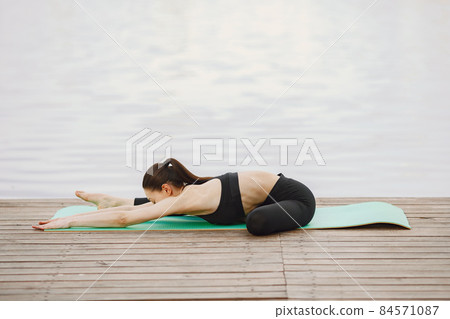 Woman practicing advanced yoga by the water 84571087