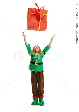 Close-up of happy little girl dressed like funny gnome or elf tossing up gift box isolated over white studio background. 84571404