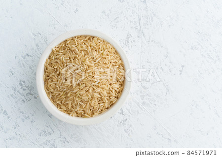 Brown rice in white bowl on white background. Dried cereals in cup, 84571971