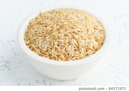 Brown rice in white bowl on white background. Dried cereals in cup, 84571972