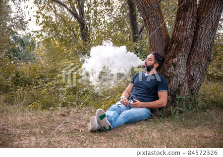 Stylish brutal man smoking an electronic cigarette. Man really likes process of smoking. Stylish brutal man smoking an electronic cigarette. Man really likes process of smoking. 84572326