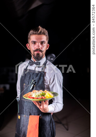 Whiskered flunkey helpfully serves cooked dish at a festive event. 84572364