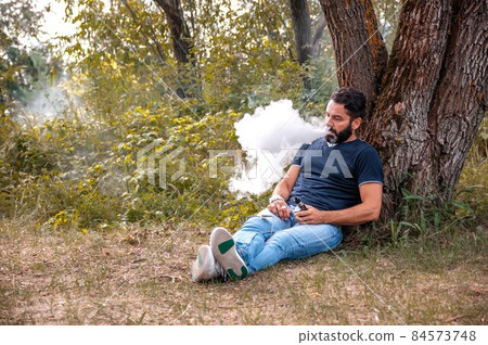 Bearded smoker blows up a couple an e-cigarette in nature. Handsome man. Bearded smoker blows up a couple an e-cigarette in nature. Handsome man. 84573748