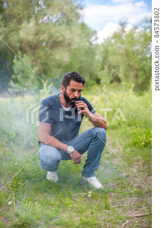 Bearded vaper smoke e-cigarette and exhals smoke cloud. Vaping. Bearded vaper smoke e-cigarette and exhals smoke cloud. Vaping. 84573802
