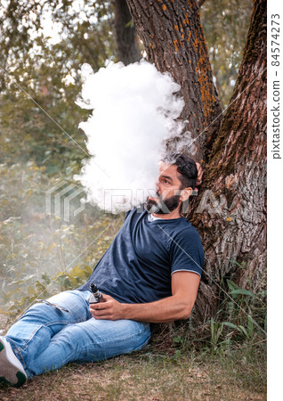 Bearded vape man blows up a couple an vape in the woods. Hybrid cigarette. 84574273