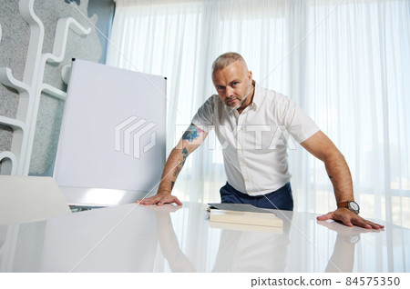 Attractive middle aged Caucasian entrepreneur, successful sales manager, businessman standing near flip chart with copy space for advertisement text, and confidently looking at camera Attractive middle aged Caucasian entrepreneur, successful sales manager, businessman standing near flip chart with copy space for advertisement text, and confidently looking at camera 84575350
