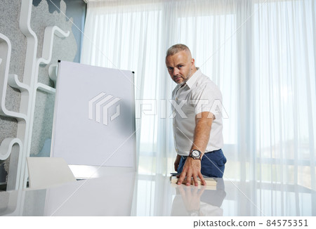 Attractive middle aged European entrepreneur, successful sales manager, businessman standing near flip chart with copy space for advertisement text, and confidently looking at camera Attractive middle aged European entrepreneur, successful sales manager, businessman standing near flip chart with copy space for advertisement text, and confidently looking at camera 84575351