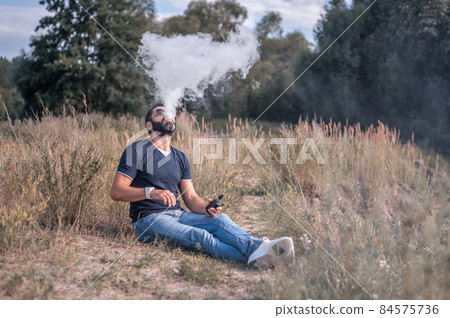 Handsome vaper exhales cloud of smoke. Vaping concept. Handsome vaper exhales cloud of smoke. Vaping concept. 84575736
