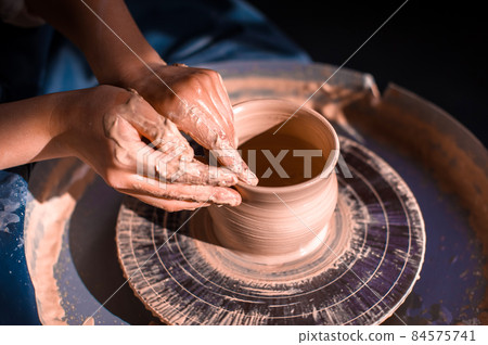 Women hands. Potter at work. Creating dishes. Potter's wheel. Dirty hands in the clay and the potter's wheel with the product. Creation. Working potter. 84575741