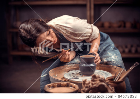 Beautiful young woman master demonstrates the process of making ceramic dishes using the old technology. Folk handicraft. 84575858