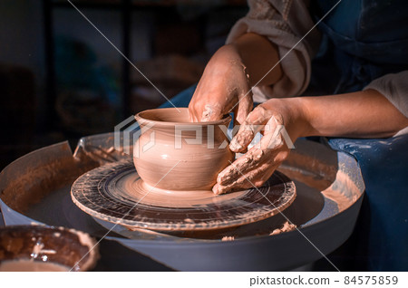 Close-up A woman potter in beautifully sculpts a deep bowl of brown clay and cuts off excess clay on a potter's wheel in a beautiful workshop Close-up A woman potter in beautifully sculpts a deep bowl of brown clay and cuts off excess clay on a potter's wheel in a beautiful workshop 84575859