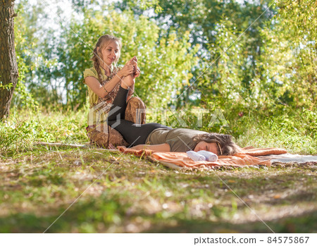 Proffesional masseuse applies her massage skills on her client on the grass of the forest. Proffesional masseuse applies her massage skills on her client on the grass of the forest. 84575867
