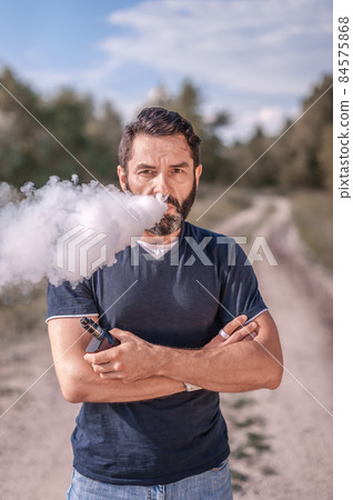 Confident vaper enjoying electronic cigarette outside. Man really likes process of smoking. Confident vaper enjoying electronic cigarette outside. Man really likes process of smoking. 84575868