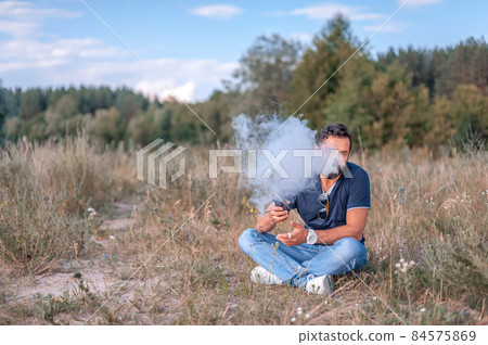 Bearded vape man enjoying an electronic cigarette in the woods. Handsome man. Bearded vape man enjoying an electronic cigarette in the woods. Handsome man. 84575869