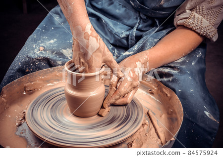 Potter's hands and potter's wheel. Close-up. 84575924