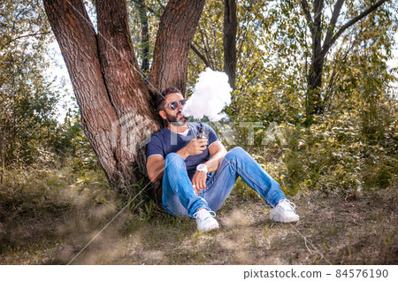 Brutal smoker exhales cloud of smoke. Hybrid cigarette. Brutal smoker exhales cloud of smoke. Hybrid cigarette. 84576190