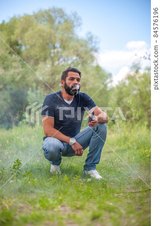 Stylish vape man with vape on the forest ground. Vaping concept. Stylish vape man with vape on the forest ground. Vaping concept. 84576196