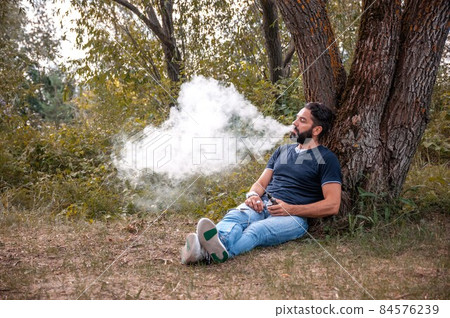 Bearded smoker enjoying an vape in the fresh air. The new technology cigarette. Bearded smoker enjoying an vape in the fresh air. The new technology cigarette. 84576239