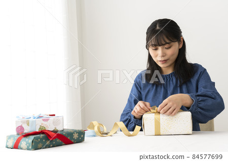 一個在包裝好的禮物上系上絲帶的女人 一個在包裝好的禮物上系上絲帶的女人 84577699