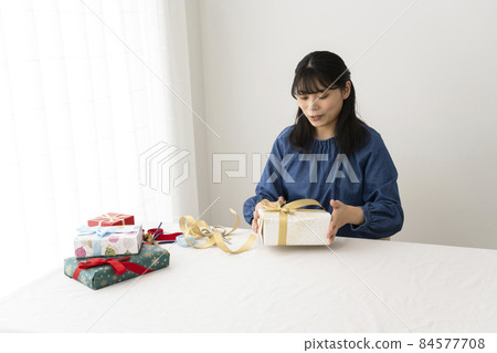 A woman who puts a ribbon on a wrapped gift A woman who puts a ribbon on a wrapped gift 84577708