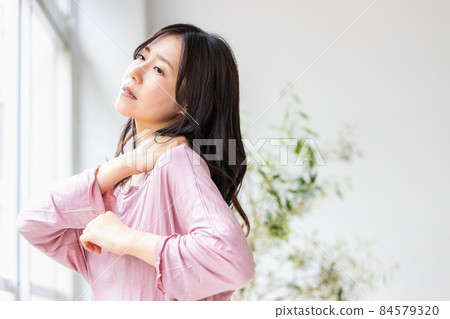 A sick woman standing by the window in the living room wearing a loungewear A sick woman standing by the window in the living room wearing a loungewear 84579320
