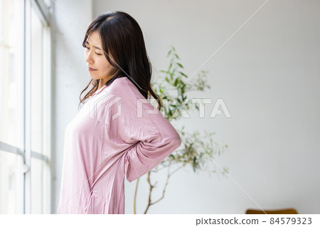 一個生病的女人站在客廳的窗戶旁，穿著家居服 84579323