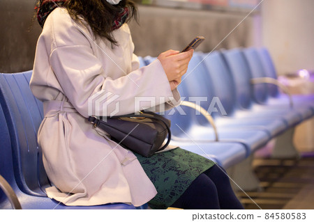 A woman looking at a mobile phone at a bus stop A woman looking at a mobile phone at a bus stop 84580583