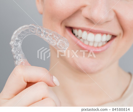 Close-up portrait of a woman putting on a transparent plastic retainer. A girl corrects a bite with the help of an orthodontic device 84580814