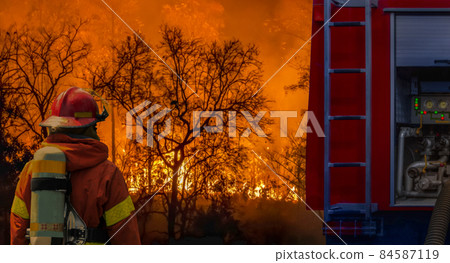 Firefighter extinguishing wildfire with fire truck Firefighter extinguishing wildfire with fire truck 84587119