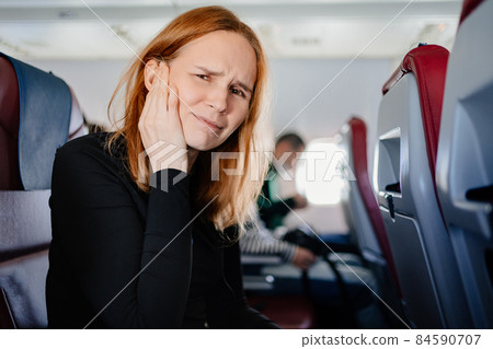 a woman on an airplane has a headache and an earache while flying on an airplane 84590707