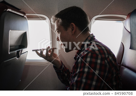 man speakerphone call on phone in seat of passenger on board of plane. 84590708