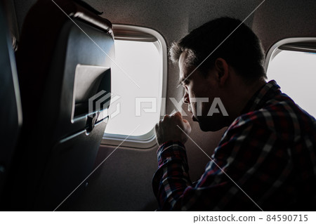 a man in a plaid shirt coughs on the plane in a window seat.  84590715