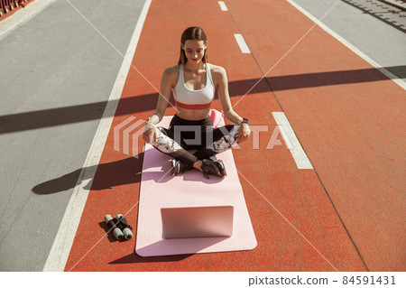 Lady ready for training watches video lesson via laptop on sportsground Lady ready for training watches video lesson via laptop on sportsground 84591431