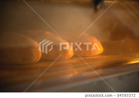 Batch of fresh buns baking in an oven viewed through the glass door with reflections in a cooking and food concept Batch of fresh buns baking in an oven viewed through the glass door with reflections in a cooking and food concept 84593372