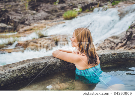Geothermal spa. Woman relaxing in hot spring pool against the background of a waterfall Geothermal spa. Woman relaxing in hot spring pool against the background of a waterfall 84593909